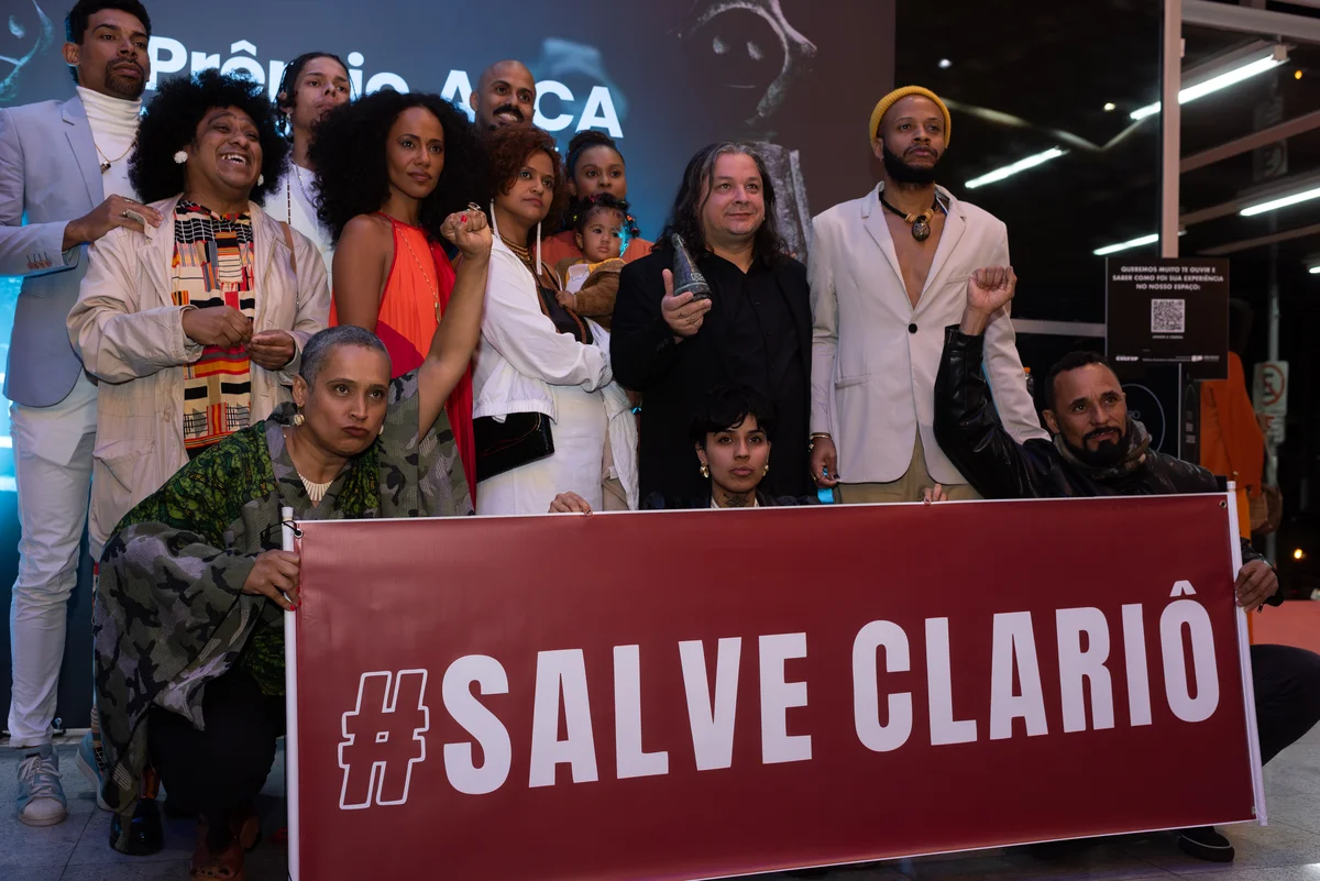 Grupo de cerca de doze pessoas posando atr&aacute;s de uma faixa vinho com os dizeres #SALVE CLARI&Ocirc;