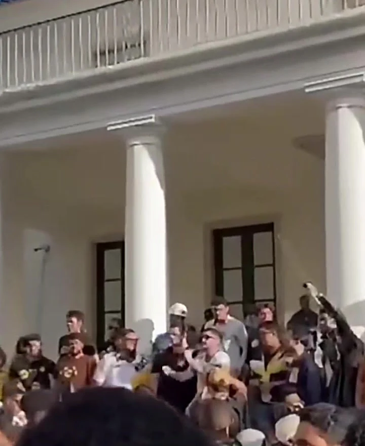 Davi Pirajá discursa ao microfone em ato de campanha na escadaria da reitoria da Ufba, cercado por apoiadores