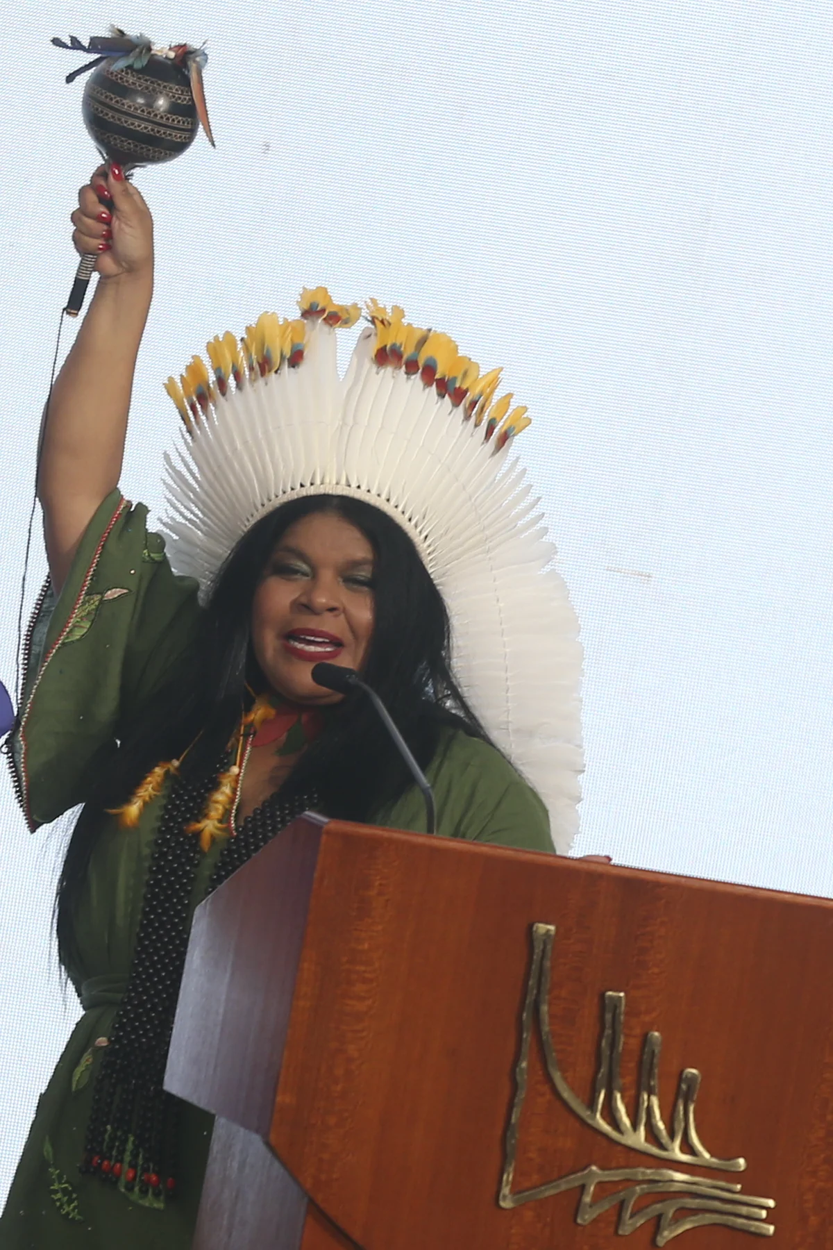 Sônia Guajajara de cocar branco atrás de um púlpito no Palácio do Planalto
