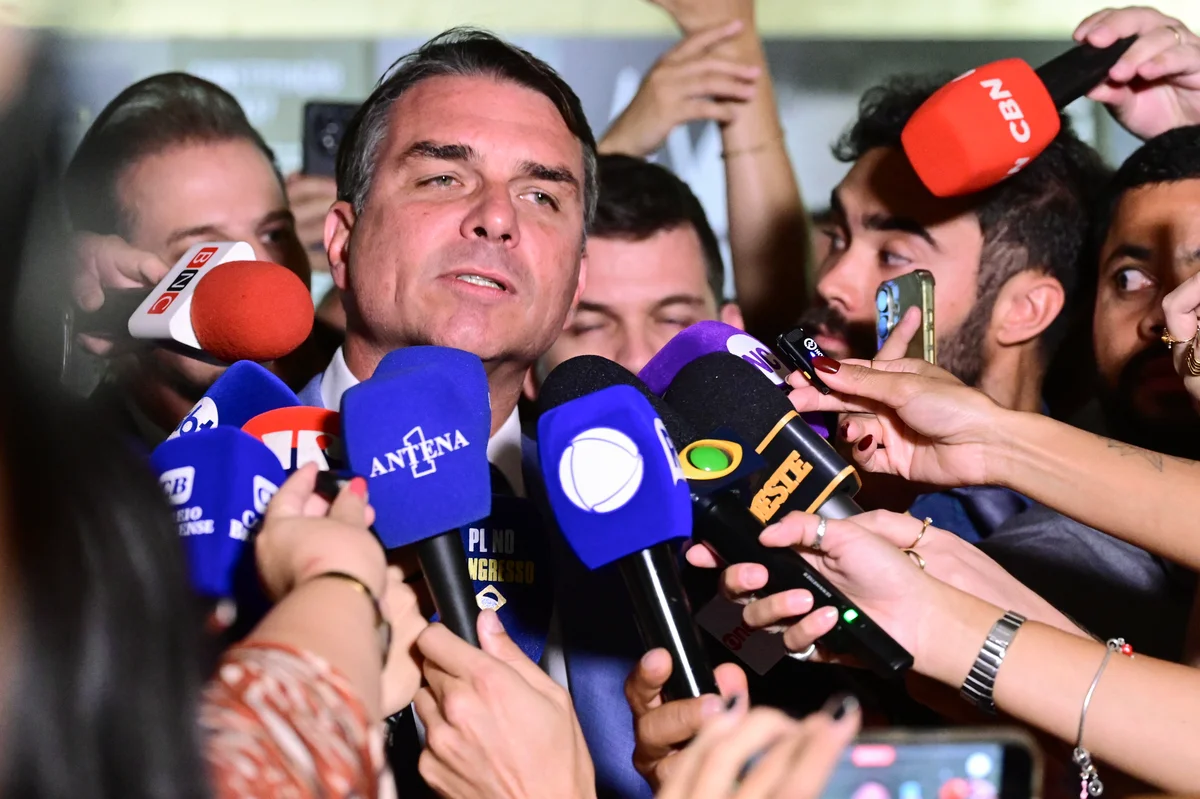 Flávio Bolsonaro fala a jornalistas, cercado de microfones de emissoras