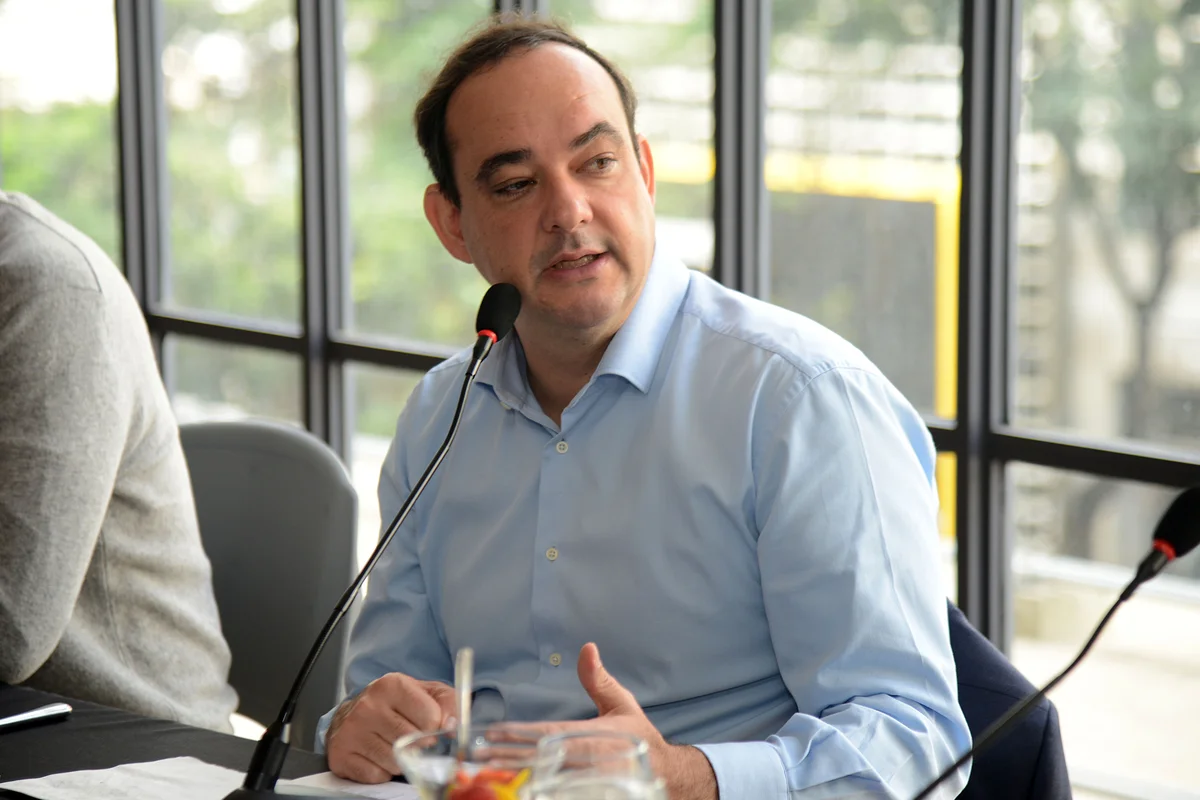 Flávio Roscoe fala ao microfone numa mesa de debate