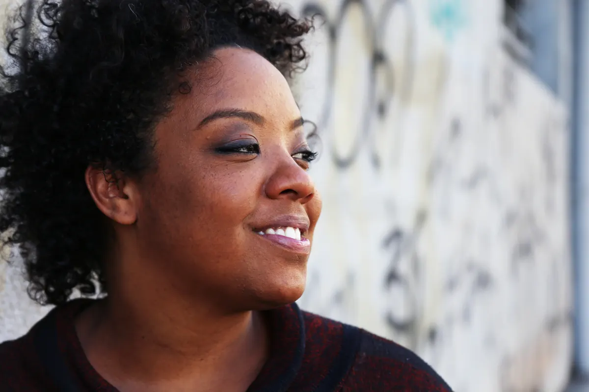 Retrato da diretora Grace Passô, de perfil, diante de um muro grafitado