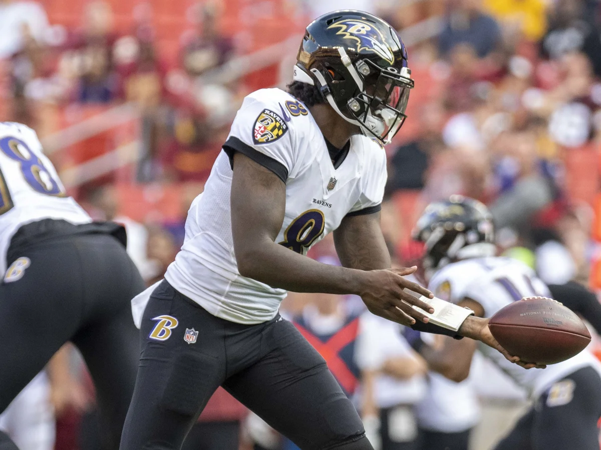 Lamar Jackson, com o uniforme branco do Baltimore Ravens, recebe a bola em campo