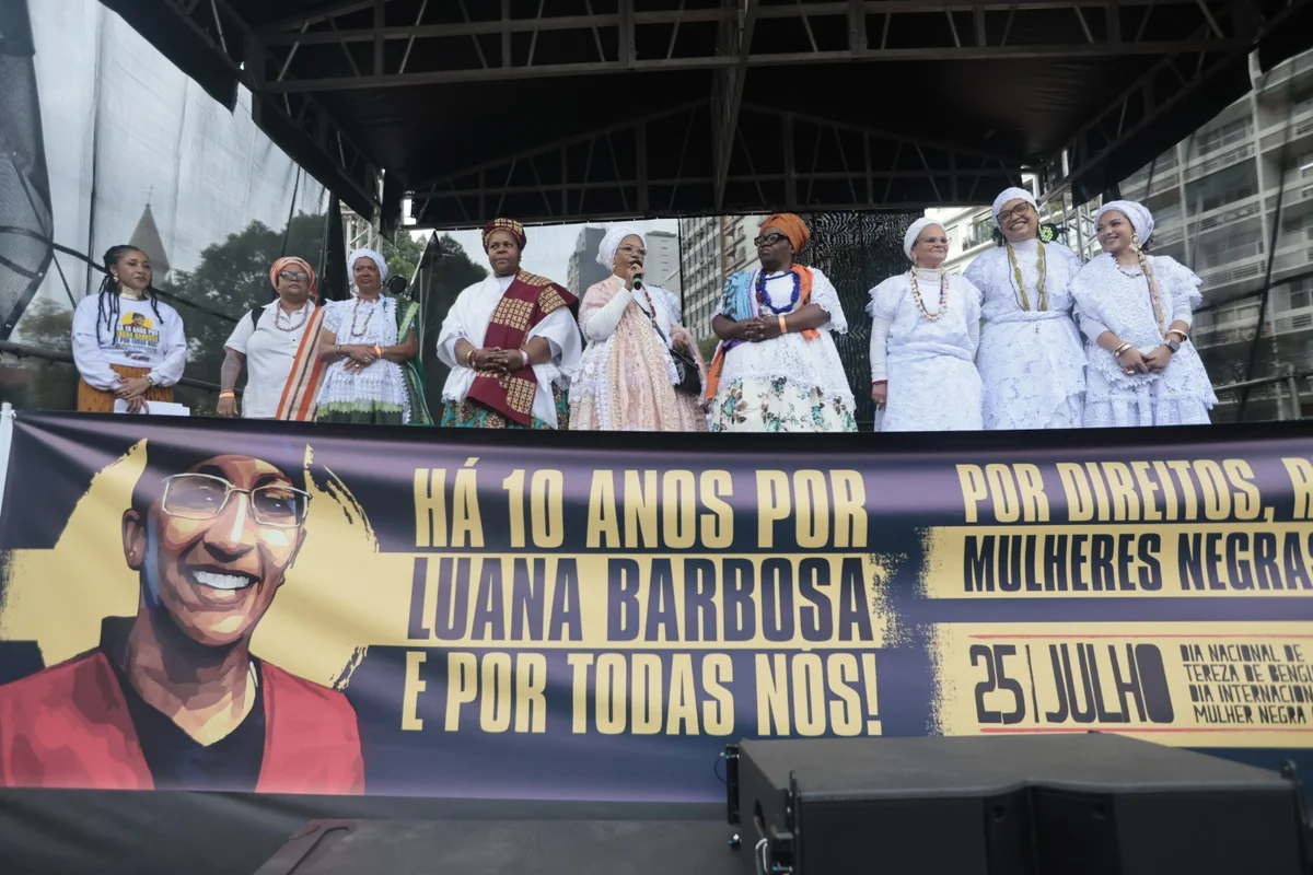 Palco da Marcha das Mulheres Negras com faixa que traz uma ilustração do rosto de Luana Barbosa