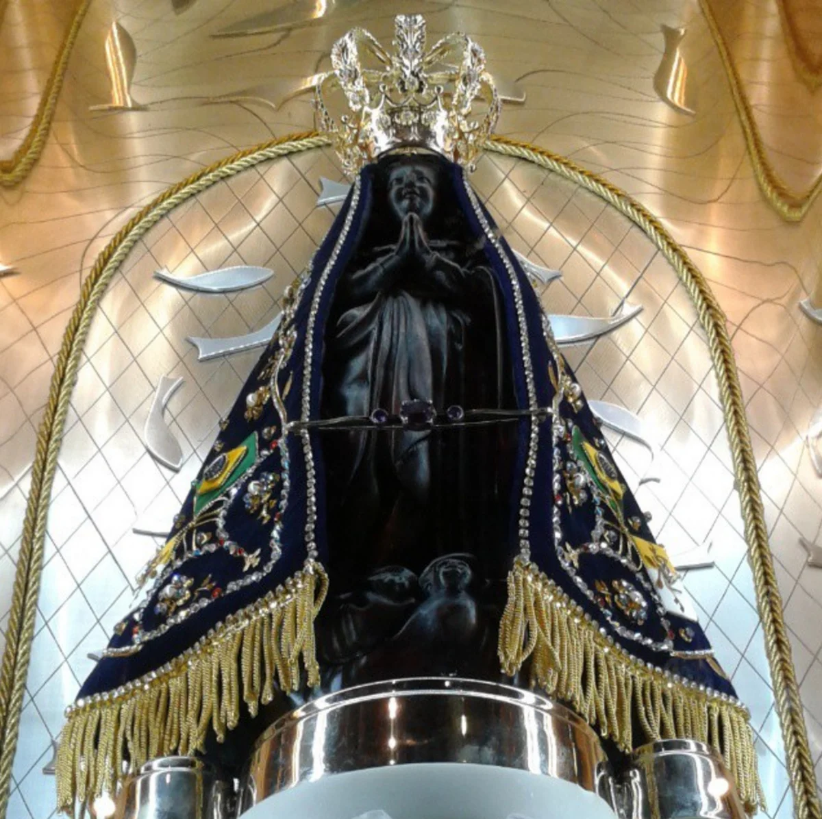 A imagem de Nossa Senhora Aparecida, escura, com manto azul bordado e coroa, no Santu&aacute;rio Nacional