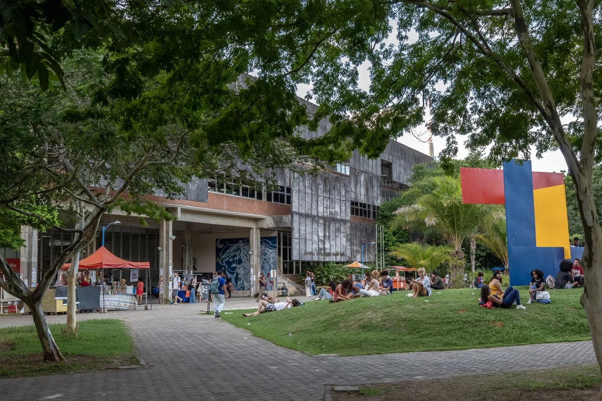 Estudantes sentados no gramado em frente ao prédio da Biblioteca Universitária Central Reitor Macedo Costa, da Universidade Federal da Bahia