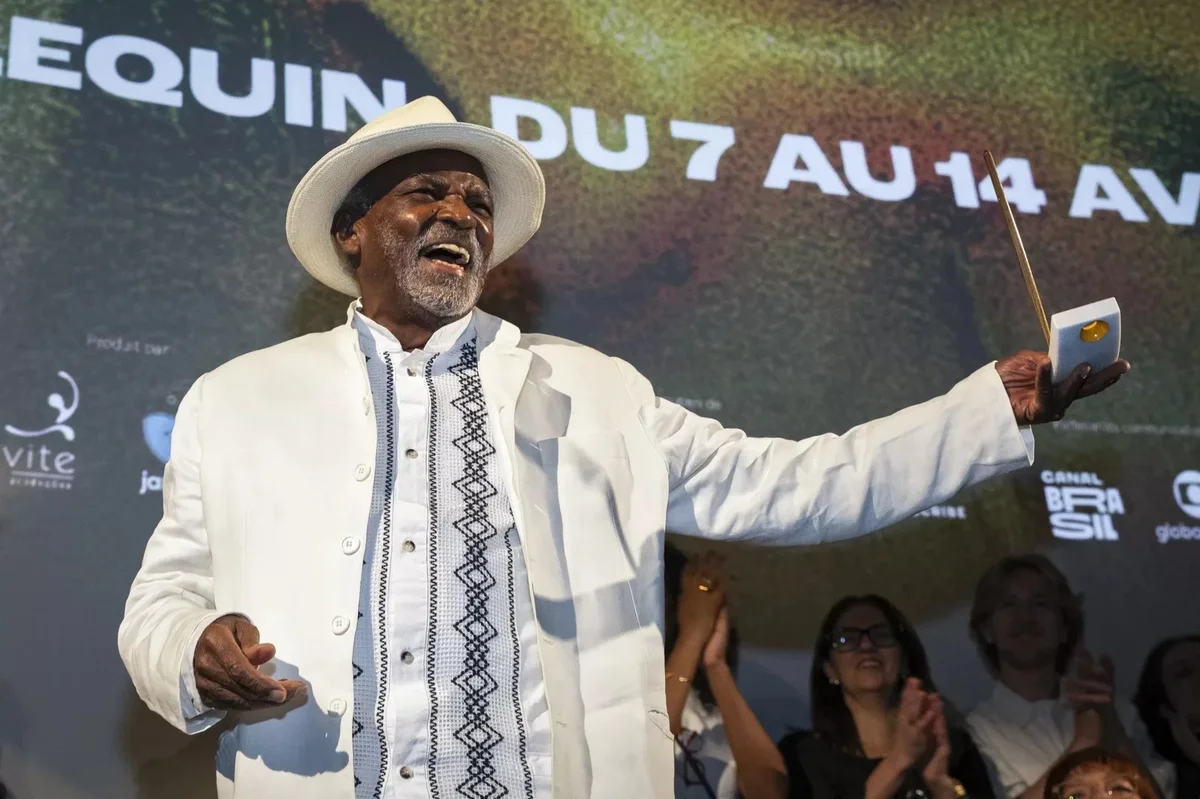 Antonio Pitanga de chapéu branco, sorrindo de braços abertos ao receber um prêmio em Paris