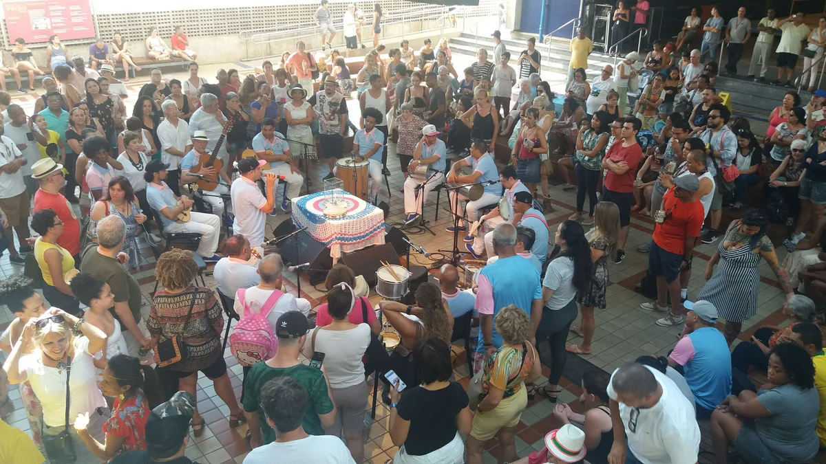 P&uacute;blico em c&iacute;rculo em volta da mesa dos m&uacute;sicos numa apresenta&ccedil;&atilde;o do Samba da Vela