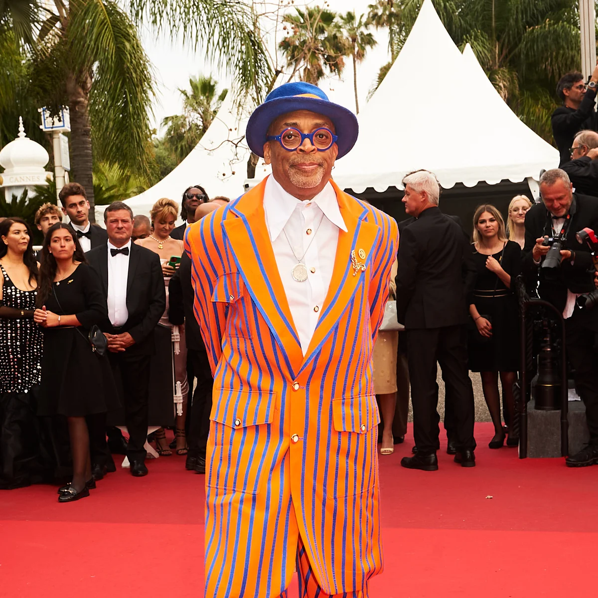 Spike Lee de terno listrado laranja e azul e chapéu azul no tapete vermelho de Cannes