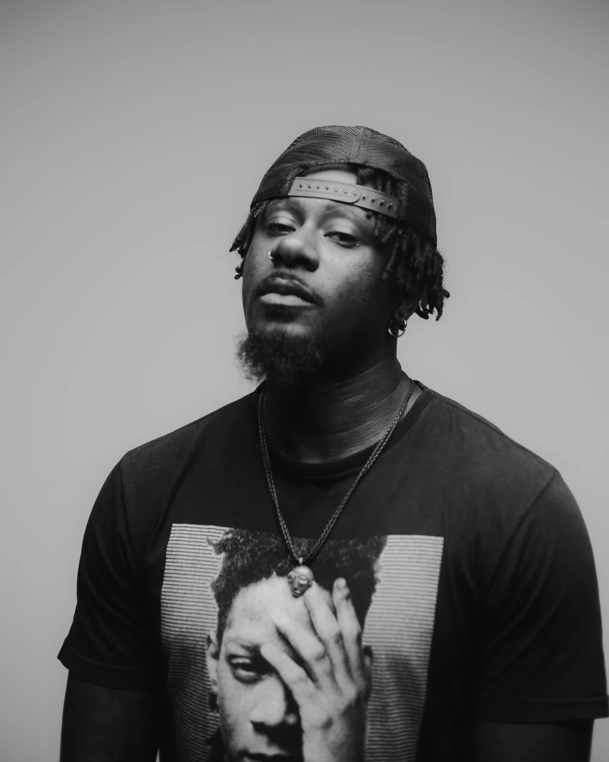 Retrato em preto e branco do rapper Zudizilla, de bon&eacute; virado para tr&aacute;s e camiseta preta